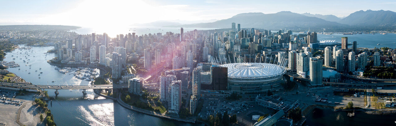 Aerial view of downtown Vancouver at golden hour — the False Creek waterfront, BC Place stadium and the North Shore mountains beyond